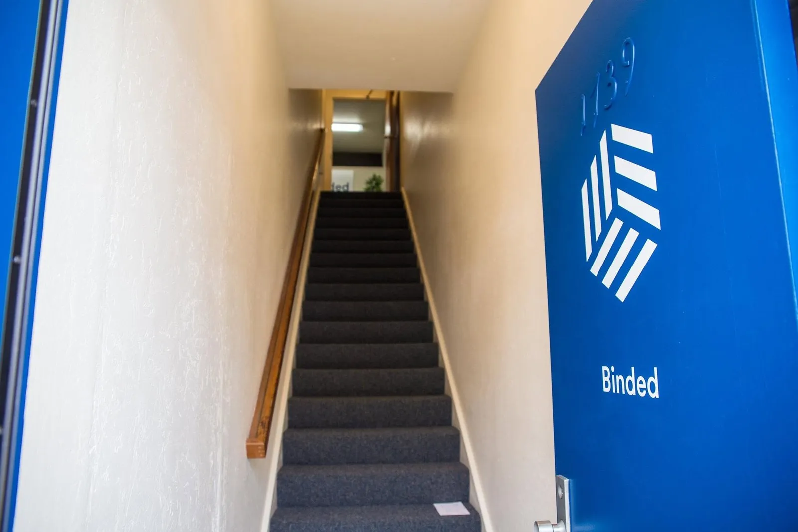 An open blue door with the Binded logo, and a staircase leading up to the office