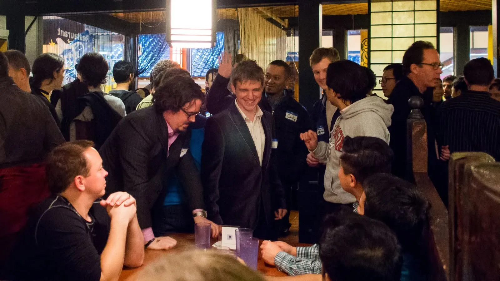 A crowded room at the Bitcoin Fair, people standing shoulder to shoulder around a table