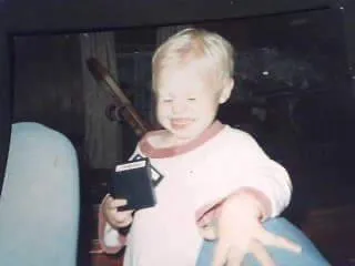 A small blond child, laughing, holding an Intellivision game cartridge
