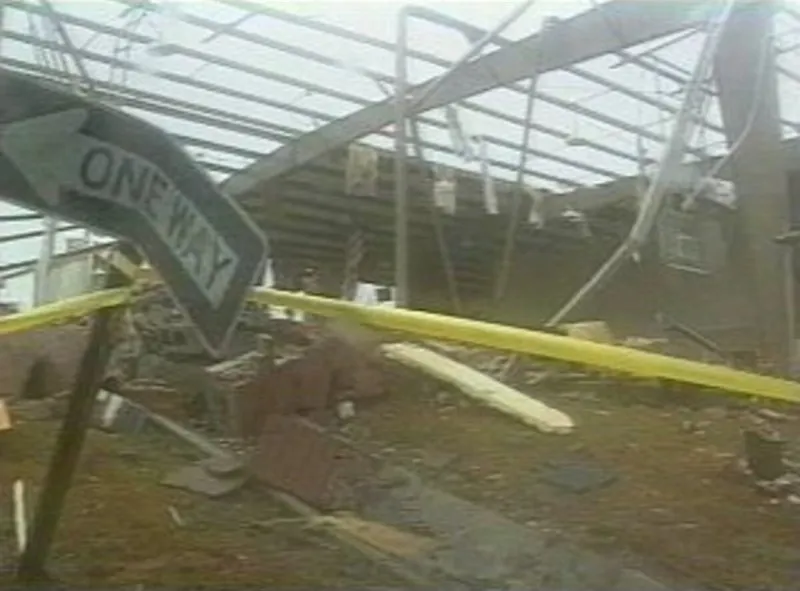 A bent one-way sign and police tape in front of a building torn open by the tornado